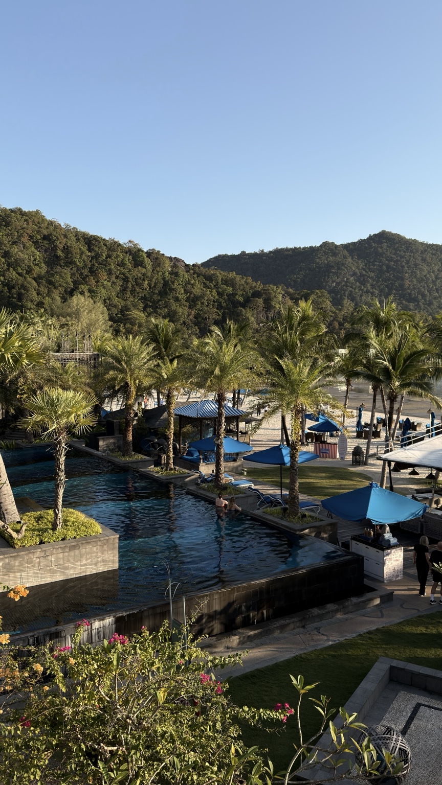 Resort swimming pools, blue parasols and palms with a beach beyond