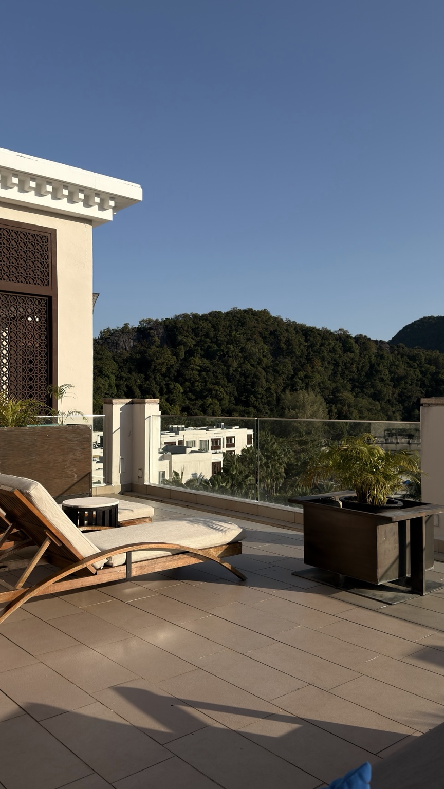 A hotel terrace with a sun lounger and a view of wooded hills